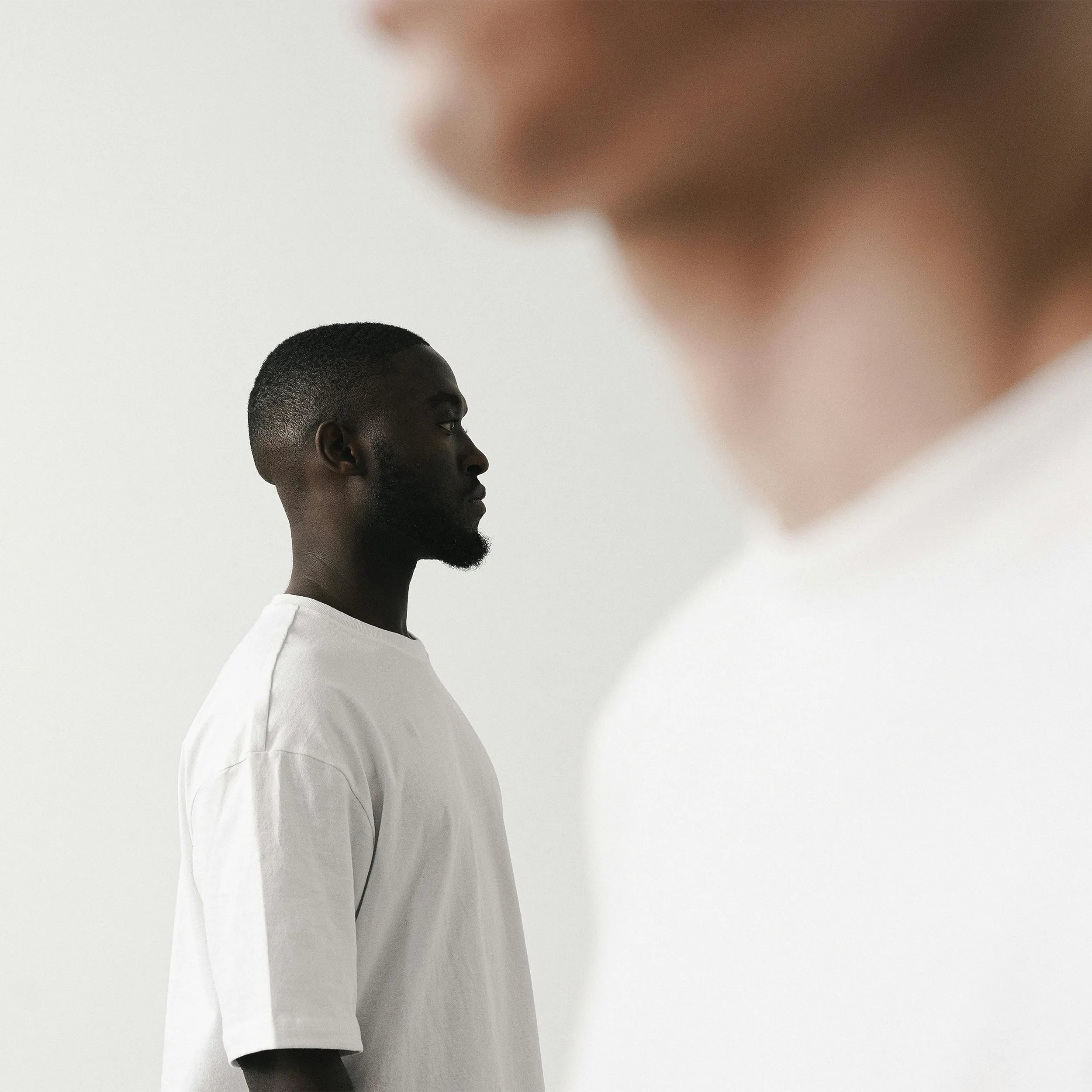 A man stands sideways, staring straight ahead with a white shirt on