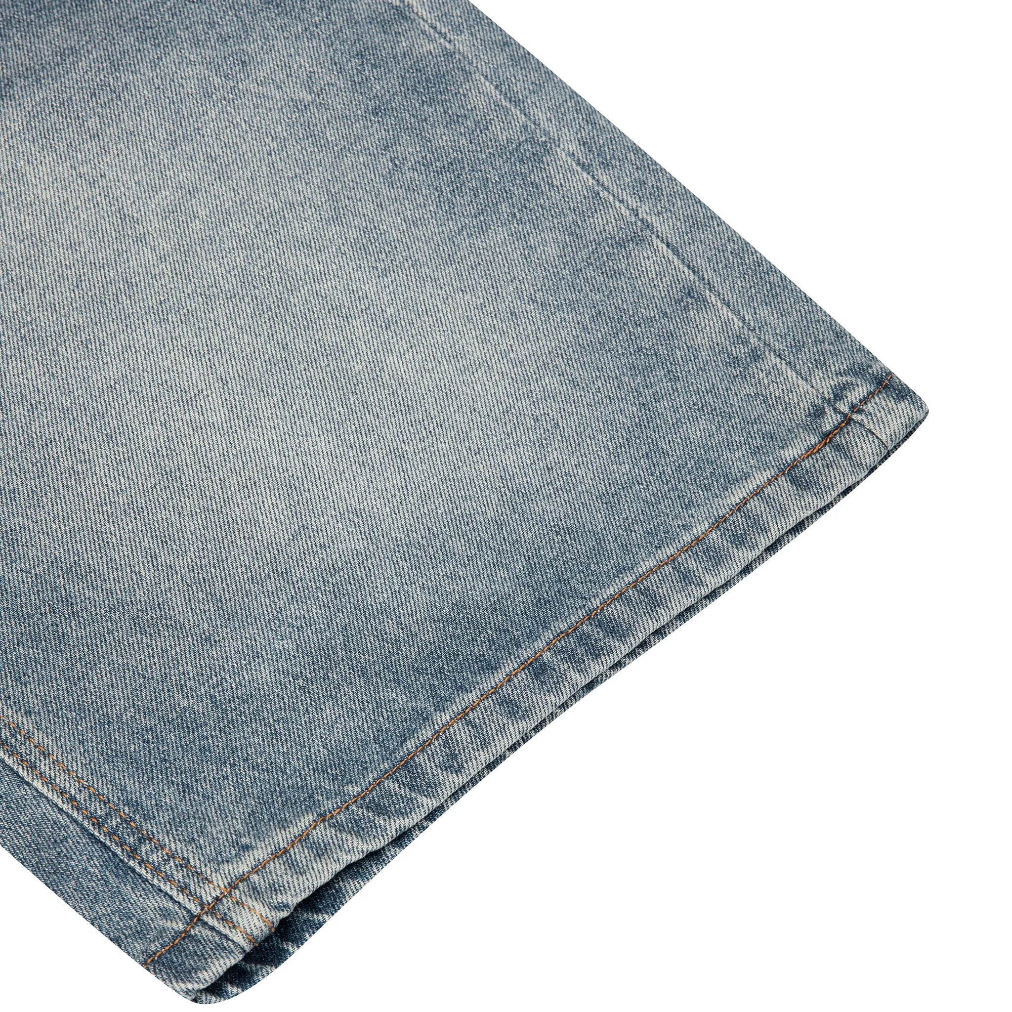 A close-up detail shot of a light blue denim fabric, showing the texture and a hemmed edge, isolated on a white background.